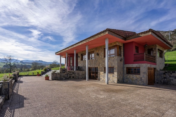 Una casa de piedra de dos pisos con techo rojo y un porche cubierto.