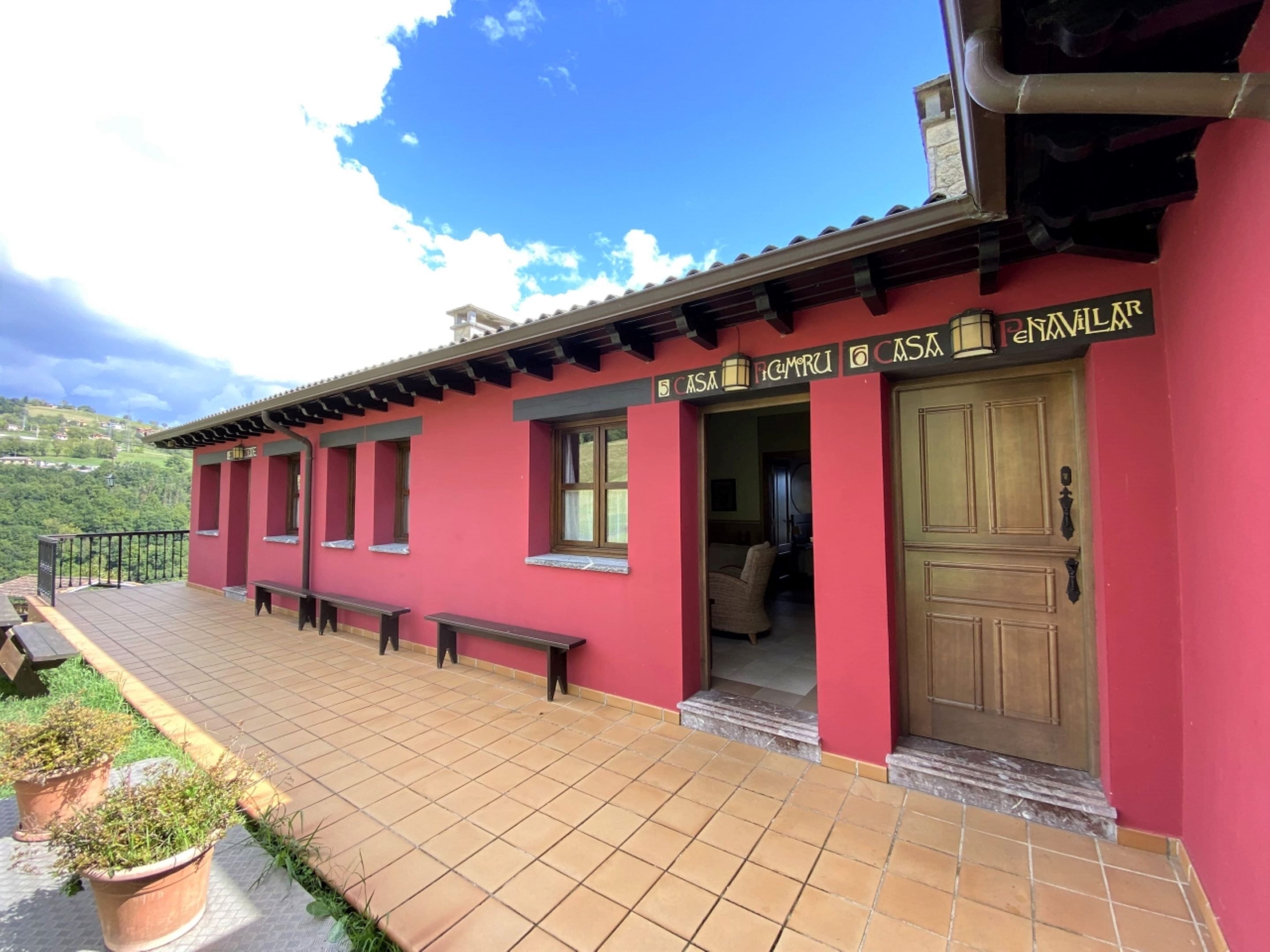 A red building with a tiled patio, a wooden door, and a bench.