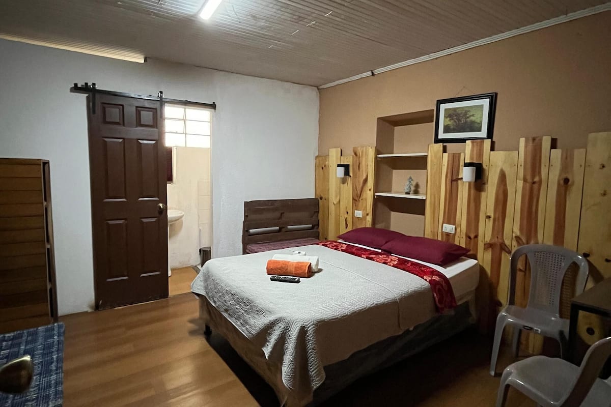 A bedroom with a wooden bed, a desk with a chair, and a wooden wardrobe.