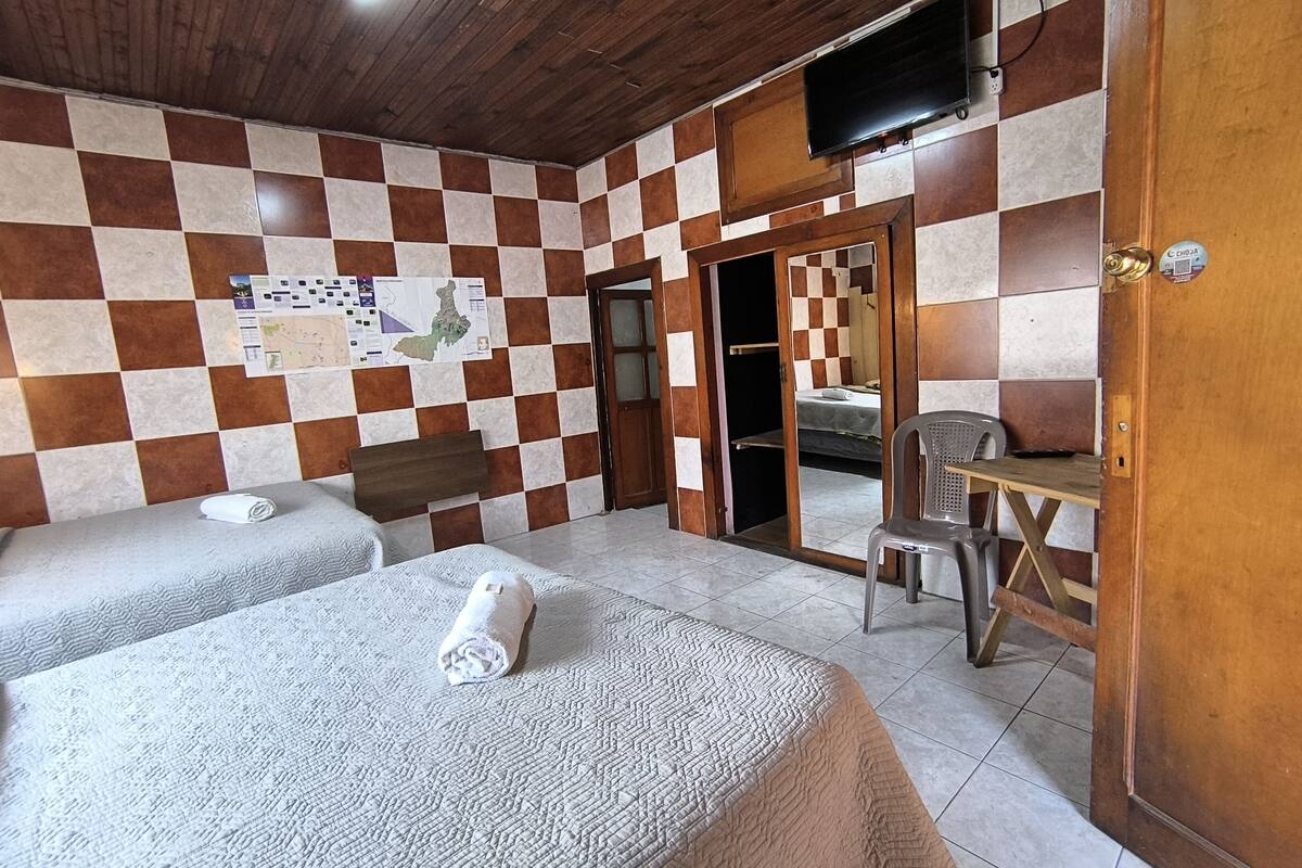 A room with two beds, a wooden ceiling, a checkered wall, a television, and a desk.