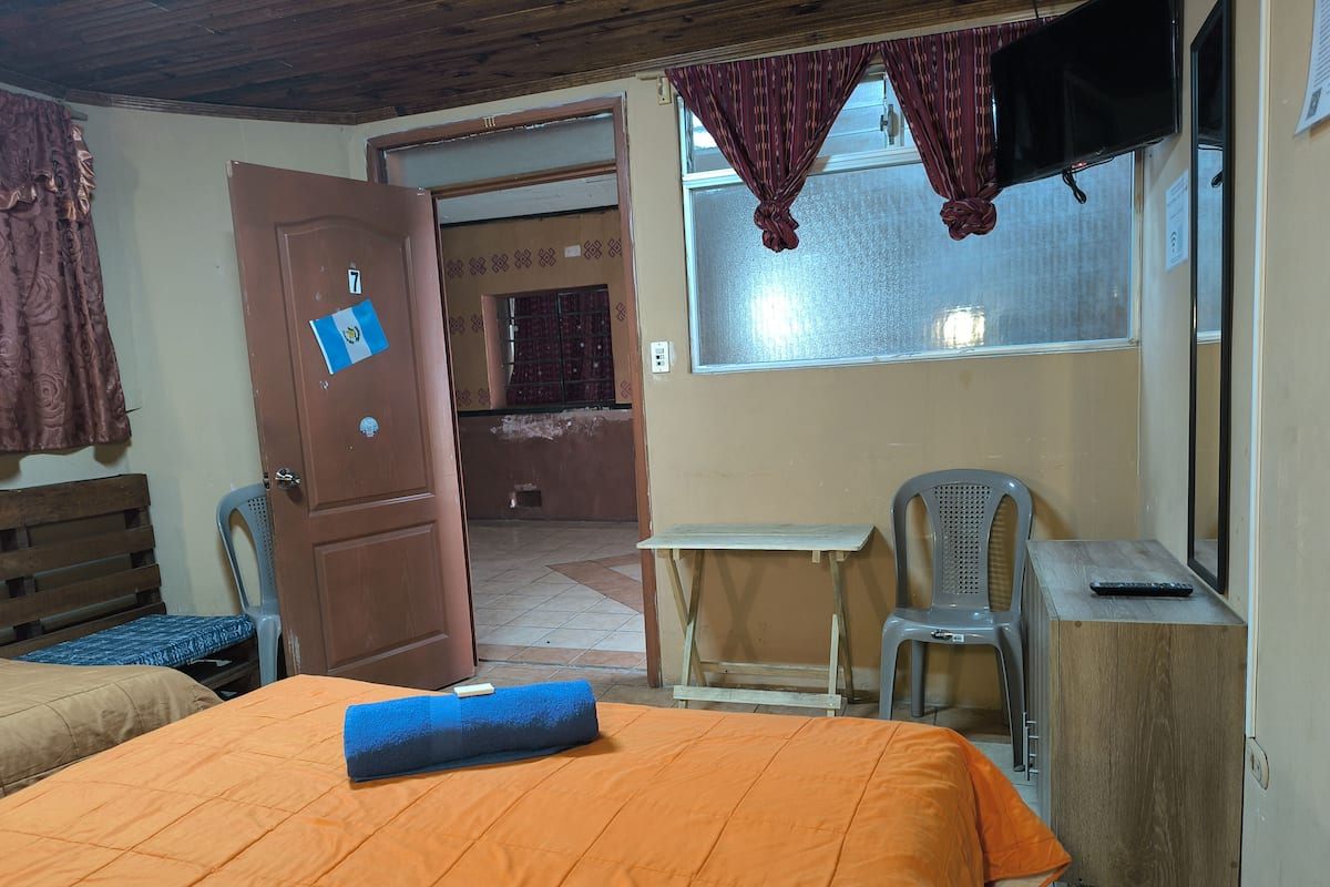 A room with a bed, a desk, a chair, a television, and a door leading to another room.
