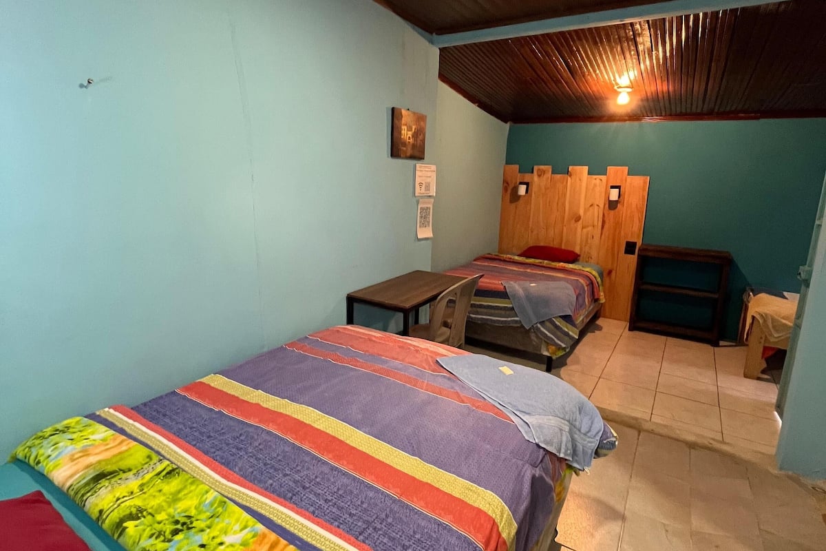 A room with two beds, a wooden ceiling, and a tiled floor.