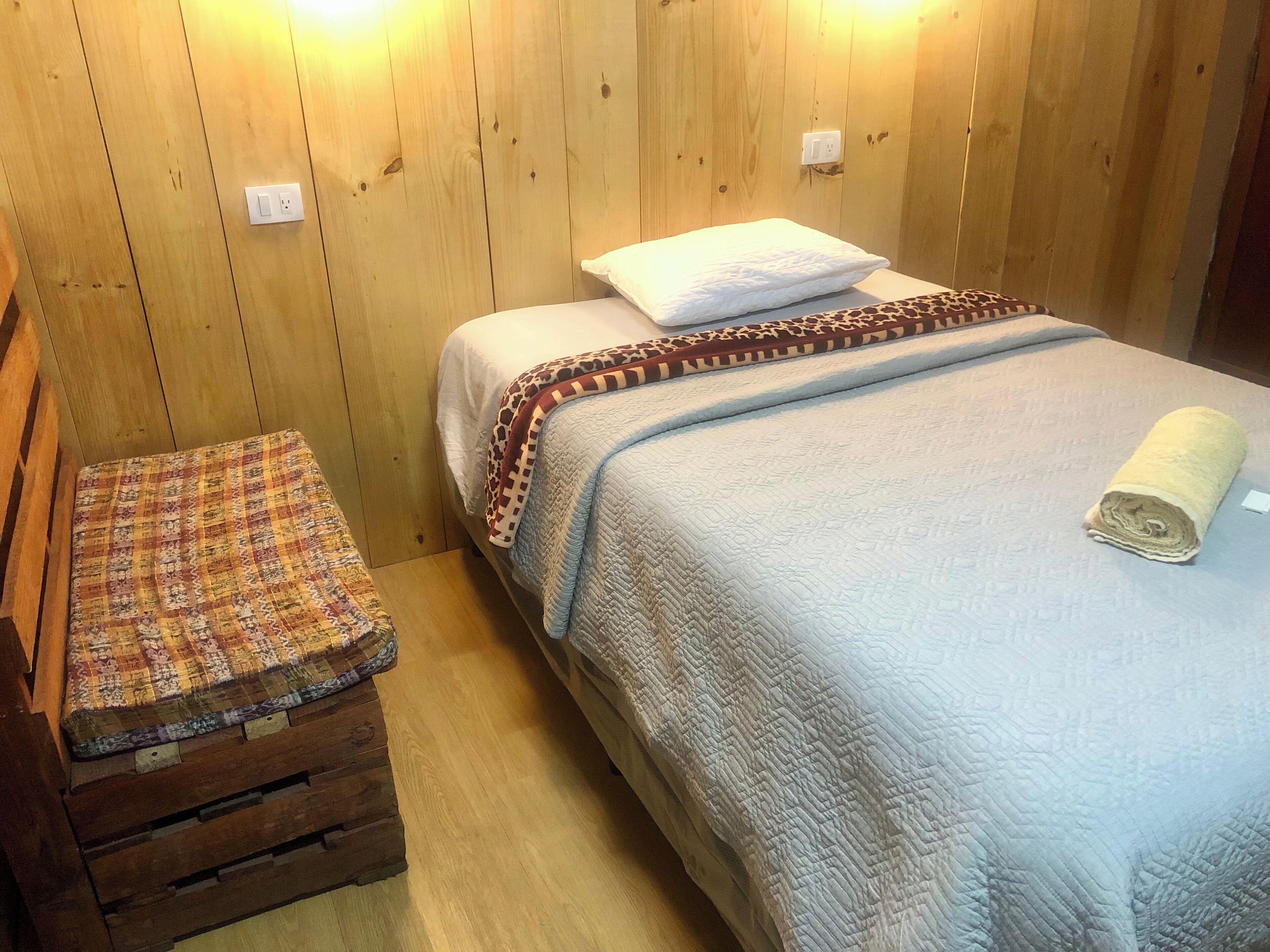 A wooden-paneled room with a bed, a bench, and a quilted blanket.
