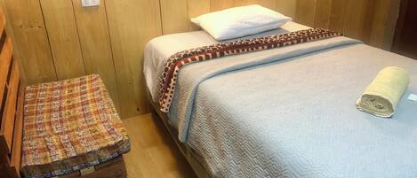 A wooden-paneled room with a bed, a bench, and a quilted blanket.
