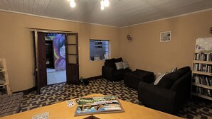 En hyggelig stue med et mønstret gulv, et træbord med et magasin, en sort sofa, en bogreol og en dør til et andet rum.