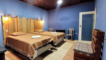 A room with two beds, a wooden headboard, two chairs, and a door.