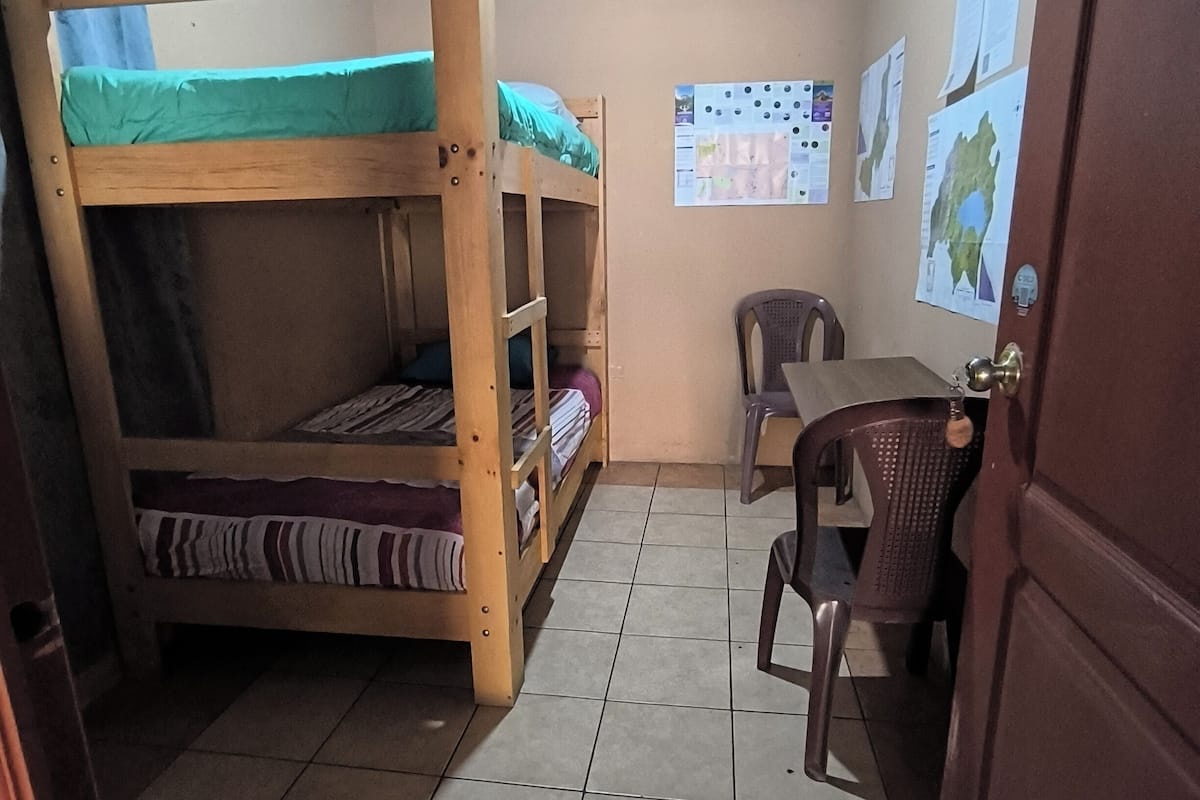 A dormitory room with bunk beds, a desk, and a chair.