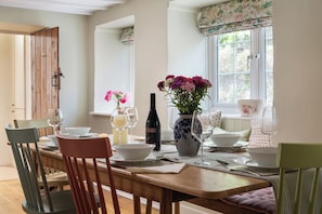 A dining table set with plates, glasses, and a bottle, surrounded by chairs. - Sharpe Cottage - large Somerset country cottage (Wiveliscombe)