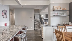Una cucina moderna con isola in marmo, sgabelli da bar e zona pranzo con sedie in legno.