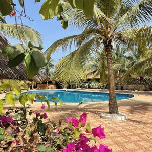 Une piscine entourée de palmiers et une structure surmontée d’un toit de chaume.
