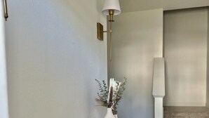 Un couloir avec un banc en bois foncé, un vase blanc orné de verdure et une lampe fixée au mur.