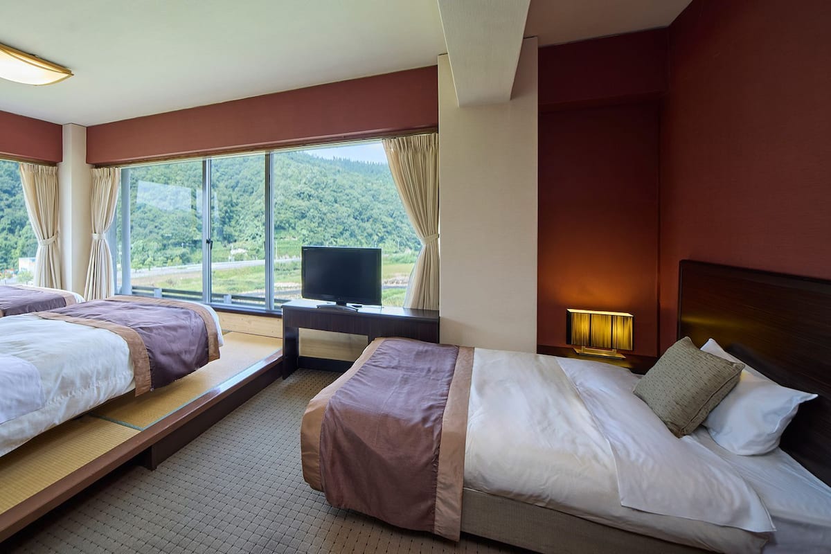 Une chambre d’hôtel avec deux lits, une télévision et de grandes fenêtres donnant sur une zone boisée.