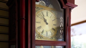 Primer plano de un reloj de pie de madera con esfera detallada y tallas ornamentales.