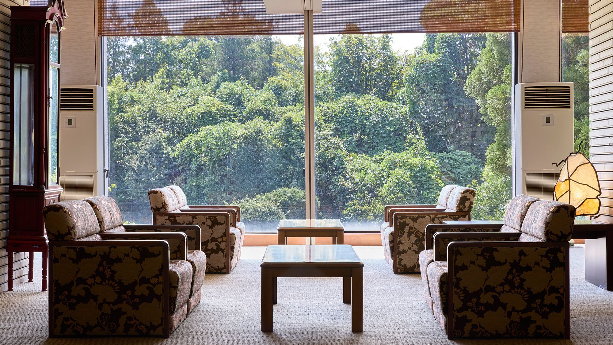 A room with a large window, a sofa set, a coffee table, and a lamp.