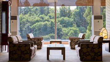 Una habitación con un ventanal grande, un conjunto de sofás, una mesa de centro y una lámpara.