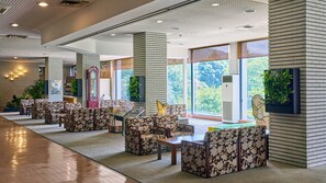 Un hall espacioso con una fila de sofás y mesas con diseños, ventanas amplias con vistas a zonas verdes y un diseño de techo moderno.