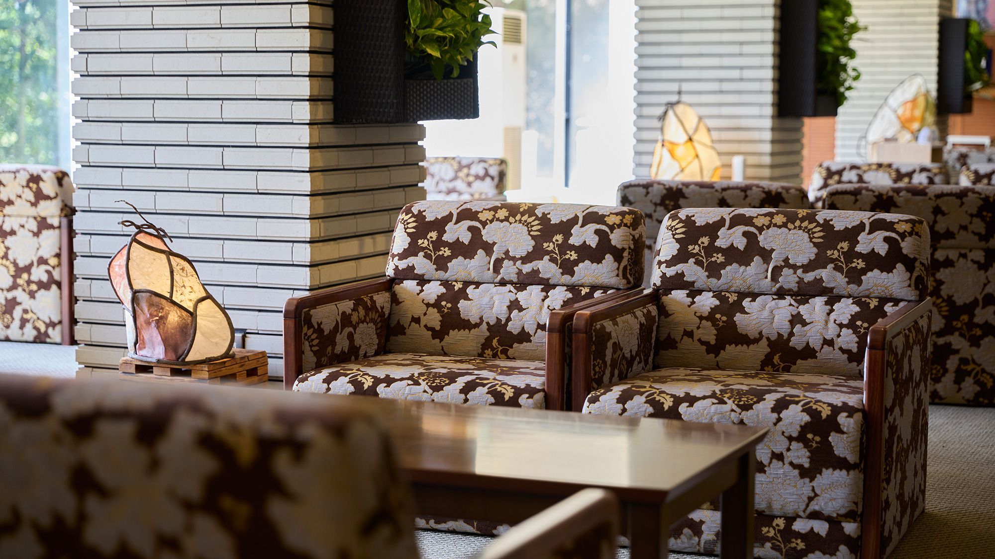 A seating area with patterned sofas and a table, a wall-mounted air conditioner, and a hanging plant.