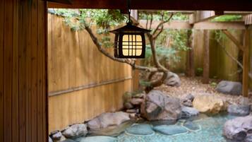 A traditional Japanese lantern hanging over a garden with a wooden fence and a rock-lined pond.