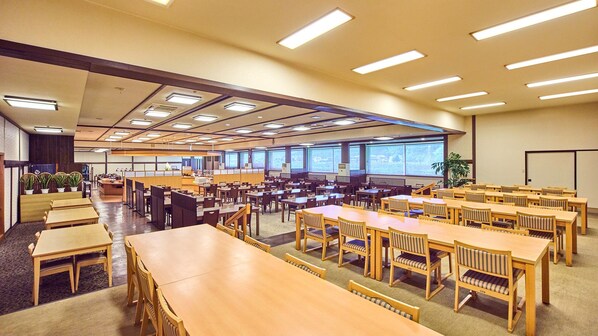 Una amplia sala de conferencias con varias mesas y sillas, ventanas grandes y un techo alto con iluminación empotrada.