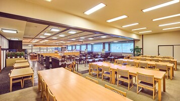 Una amplia sala de conferencias con varias mesas y sillas, ventanas grandes y un techo alto con iluminación empotrada.