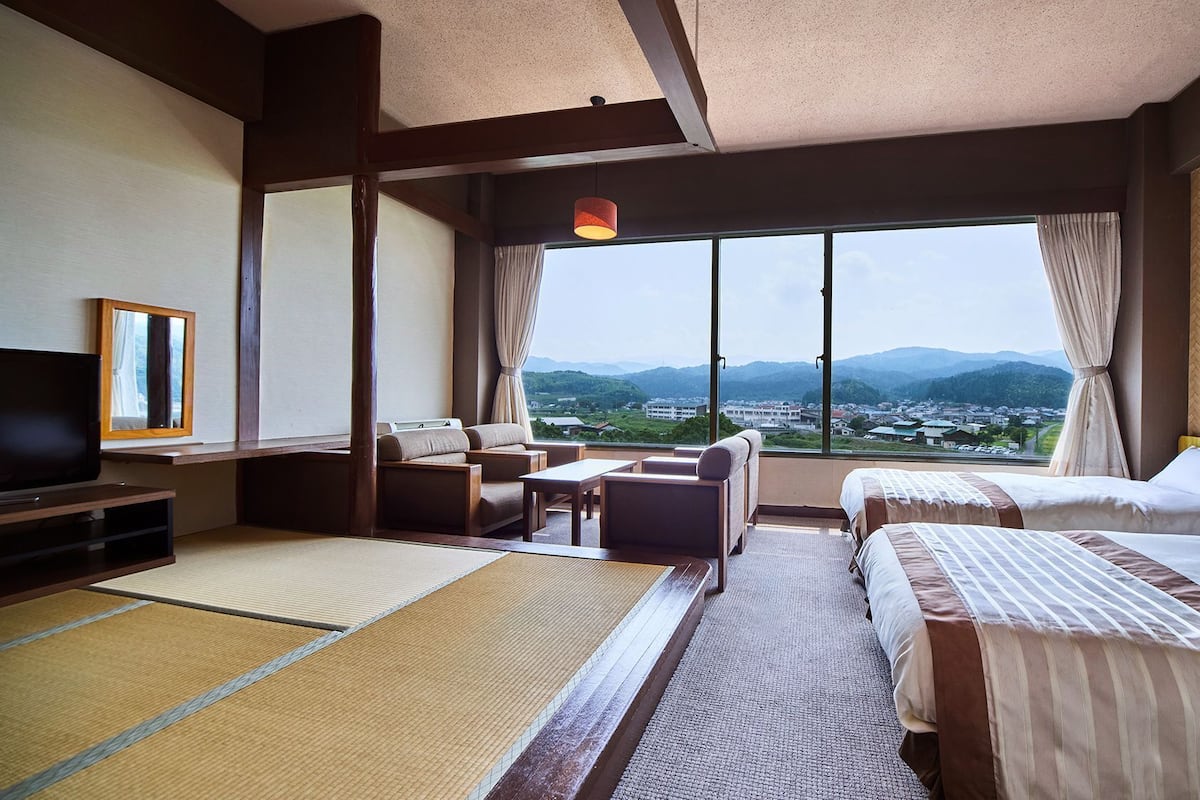 Une chambre d’hôtel dotée d’une grande fenêtre, d’un canapé, d’un lit, d’une télévision et offrant une vue sur la ville et les montagnes.
