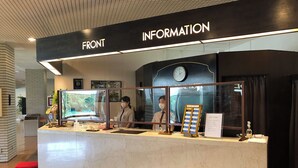 Un mostrador de recepción con un reloj, marcos con fotografías y un cartel que indica 'INFORMATION' y 'FRONT'.