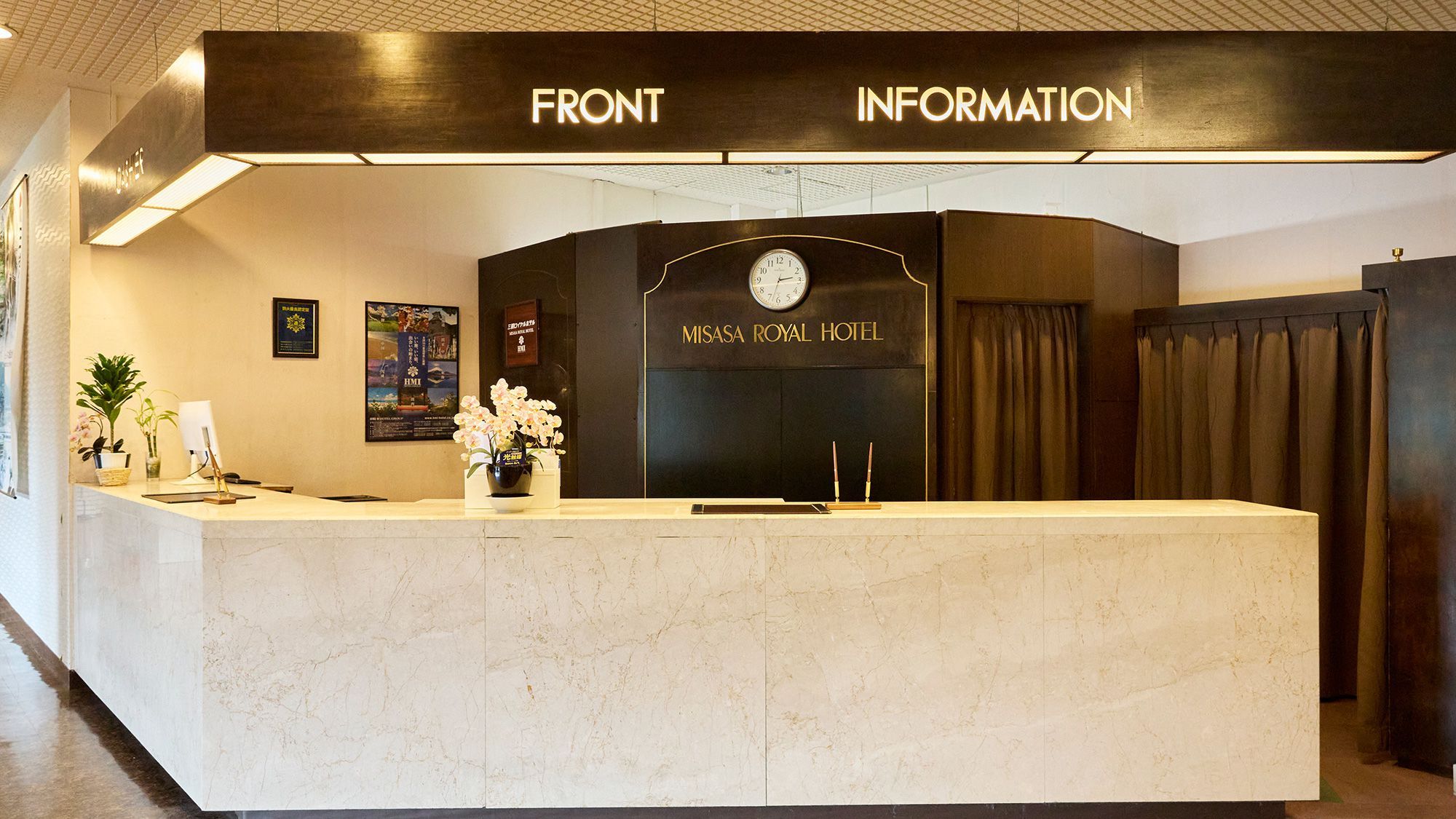 A reception desk with a clock and a sign for 'MISASA ROYAL HOTEL' above it.