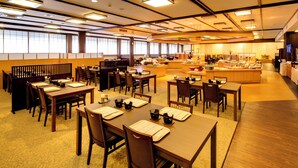 Un comedor de hotel con varias mesas y sillas, una estación de buffet y un mostrador de recepción.