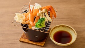 Una cesta de mimbre con mariscos y verduras, una taza de cerámica con salsa de soja, y un posavasos de madera.