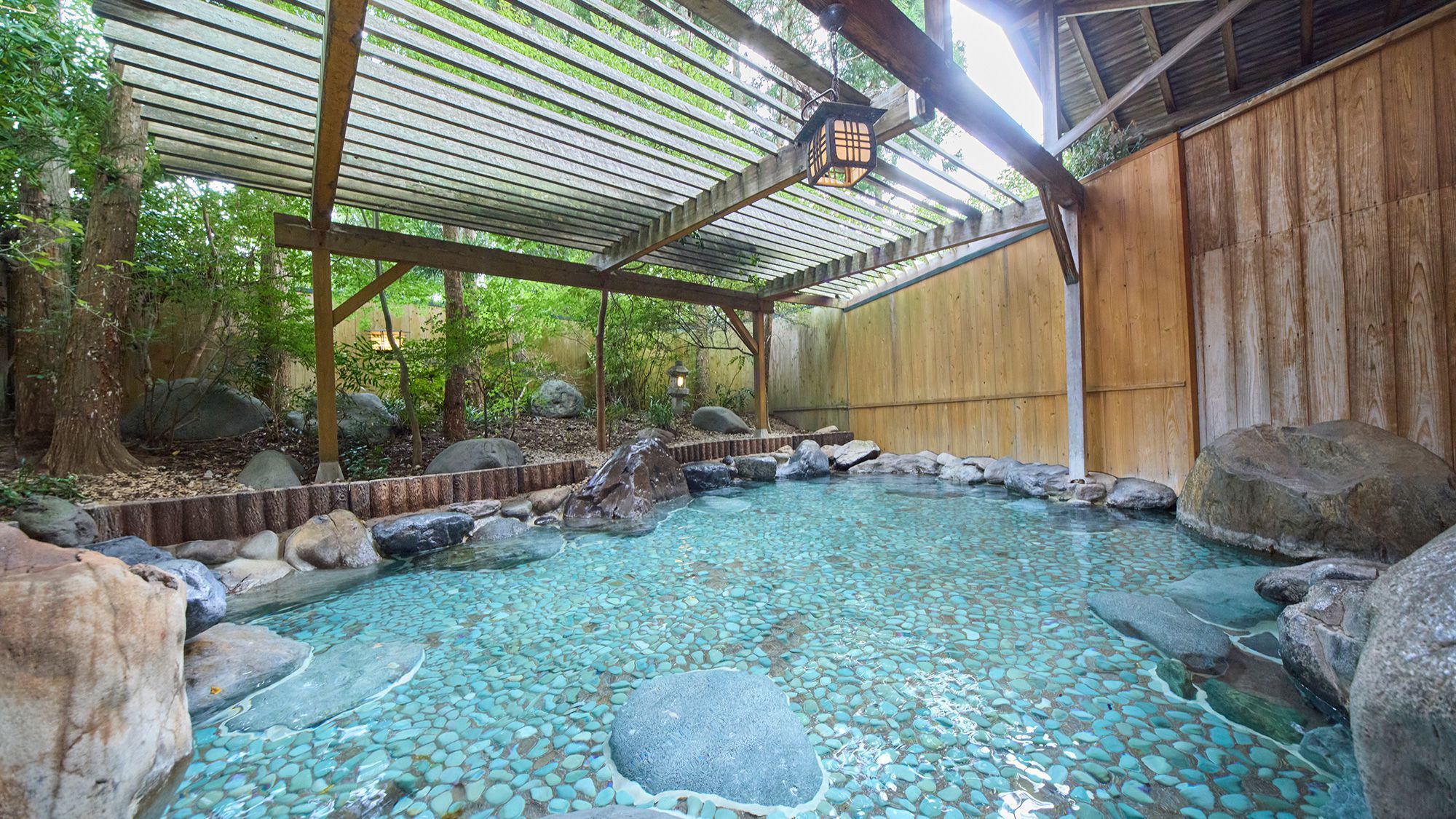 A hot spring area with a wooden structure, rocks, and a tiled floor.