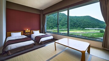 Habitación de hotel con dos camas, una mesita y vista a un paisaje boscoso.