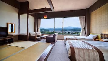 A hotel room with a large window, a sofa, a bed, a TV, and a view of a town and mountains.
