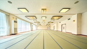 A long, empty hotel room with a tatami mat floor, large windows, and a row of doors along one wall. - Misasa Royal Hotel (Misasa)