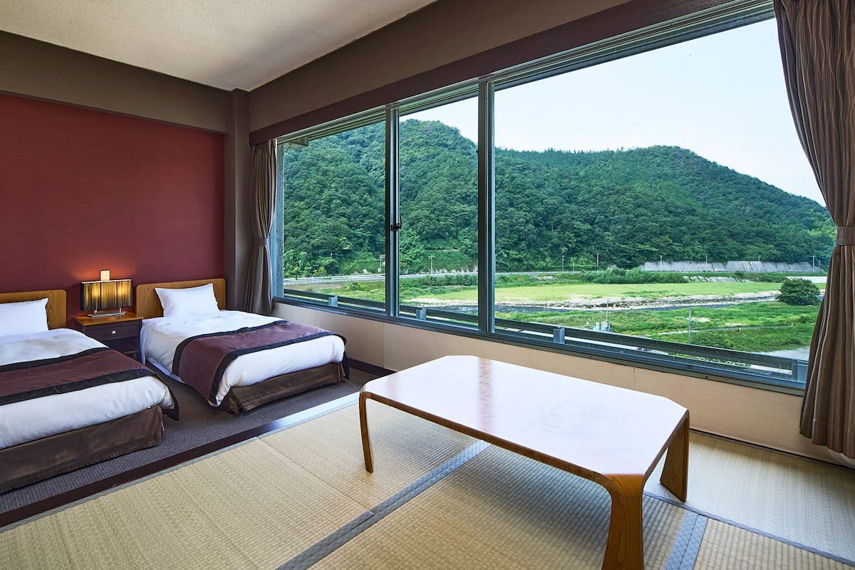 Une chambre d’hôtel avec deux lits, une table et une grande fenêtre donnant sur une zone boisée.