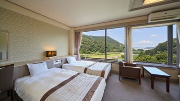 Habitación de hotel con dos camas, un escritorio y vistas a un paisaje verde.