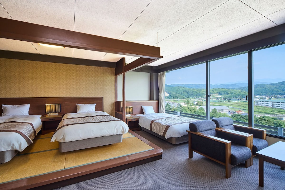 Une chambre d’hôtel avec deux lits, un canapé, une table et une grande fenêtre donnant sur la ville.