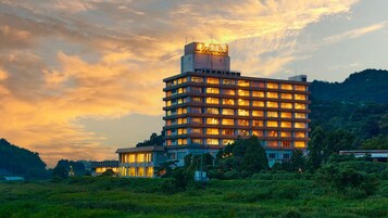 Un hotel de varios pisos con un letrero llamativo en la parte superior, rodeado de vegetación y colinas.