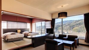 Habitación de hotel con cama, sofá, televisión y vistas a montañas.