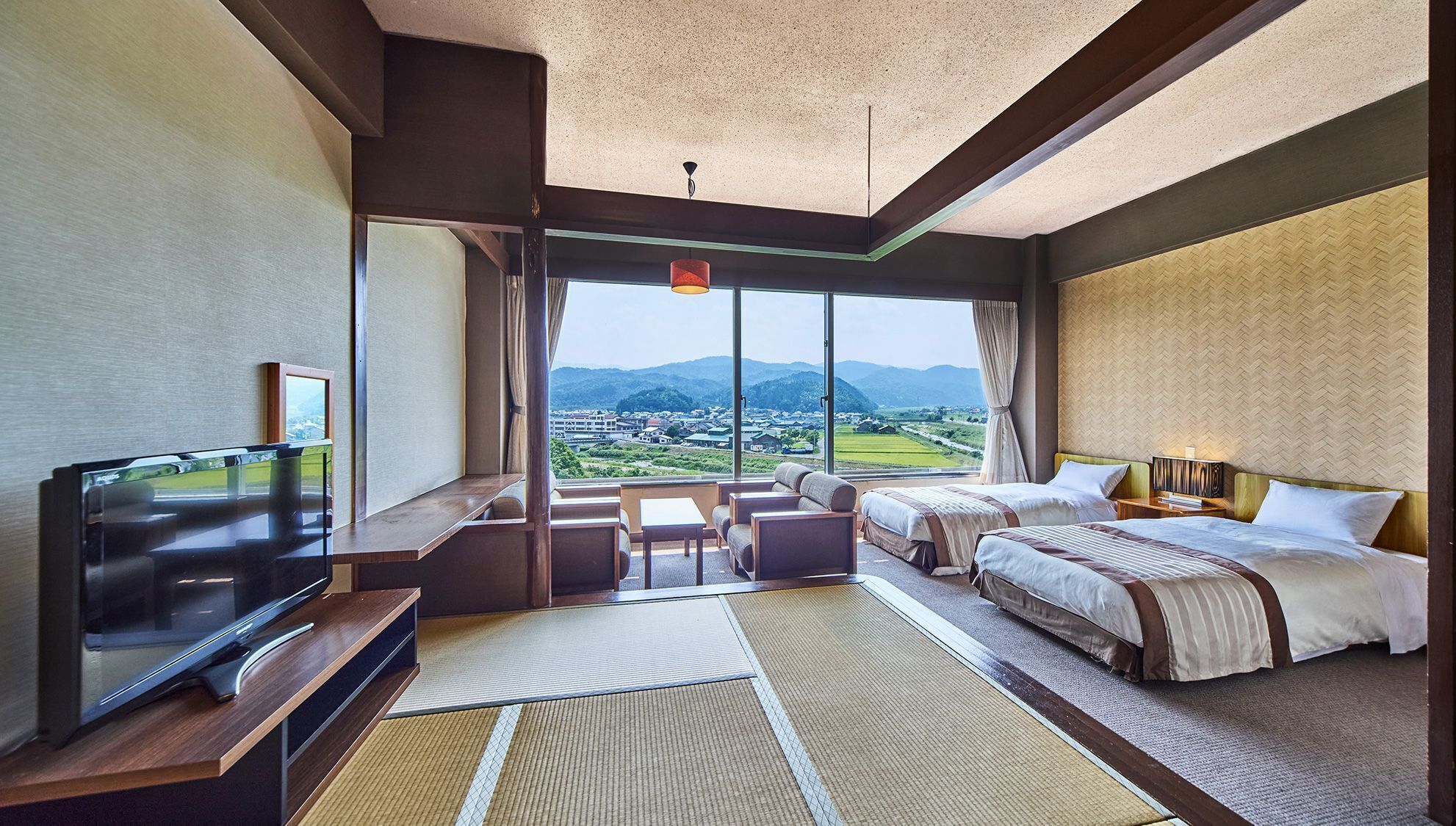 A hotel room with a large window, a flat-screen TV, two beds, a sofa, and a small table.