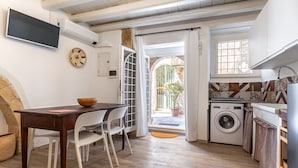 A compact kitchen with a washing machine, a dining area with a table and chairs, and a large window with a view of the outside. - Il Cortile sul Vicolo Alla Giudecca by Wonderful Italy (Syracuse)