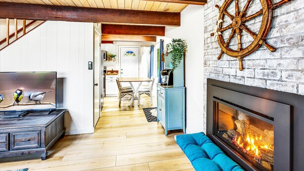 A modern living room with a fireplace, wooden beams, and a ship's wheel decoration. - Captain Green s Cabin (Copalis Beach)