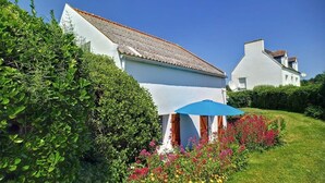 A white house with a tiled roof, surrounded by lush greenery and colorful flowers. - Tipoz'Immo • Brise Marine 2 • beach 600 m away • ideal for couples or families! (Plozévet)