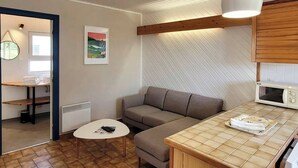 A compact living space with a sofa, a small round table, a microwave, and a hanging light fixture. - Tipoz'Immo • Brise Marine 2 • beach 600 m away • ideal for couples or families! (Plozévet)