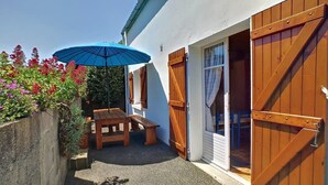 A patio with a wooden table and chairs, a blue umbrella, and a concrete wall with plants. - Tipoz'Immo • Brise Marine 2 • beach 600 m away • ideal for couples or families! (Plozévet)