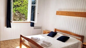 A bedroom with a wooden bed, white walls, a window with curtains, and a radiator. - Tipoz'Immo • Brise Marine 2 • beach 600 m away • ideal for couples or families! (Ploz évet)