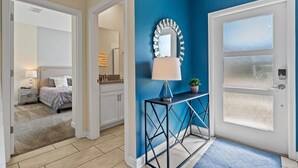 A hallway with a blue accent wall, a mirror, and a door with frosted glass panels. - Champions Gate Oasis 4BR Vacation Haven (Davenport)