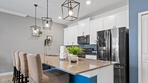 A modern kitchen with white cabinets, a stainless steel refrigerator, and a blue accent wall. - Champions Gate Oasis 4BR Vacation Haven (Davenport)