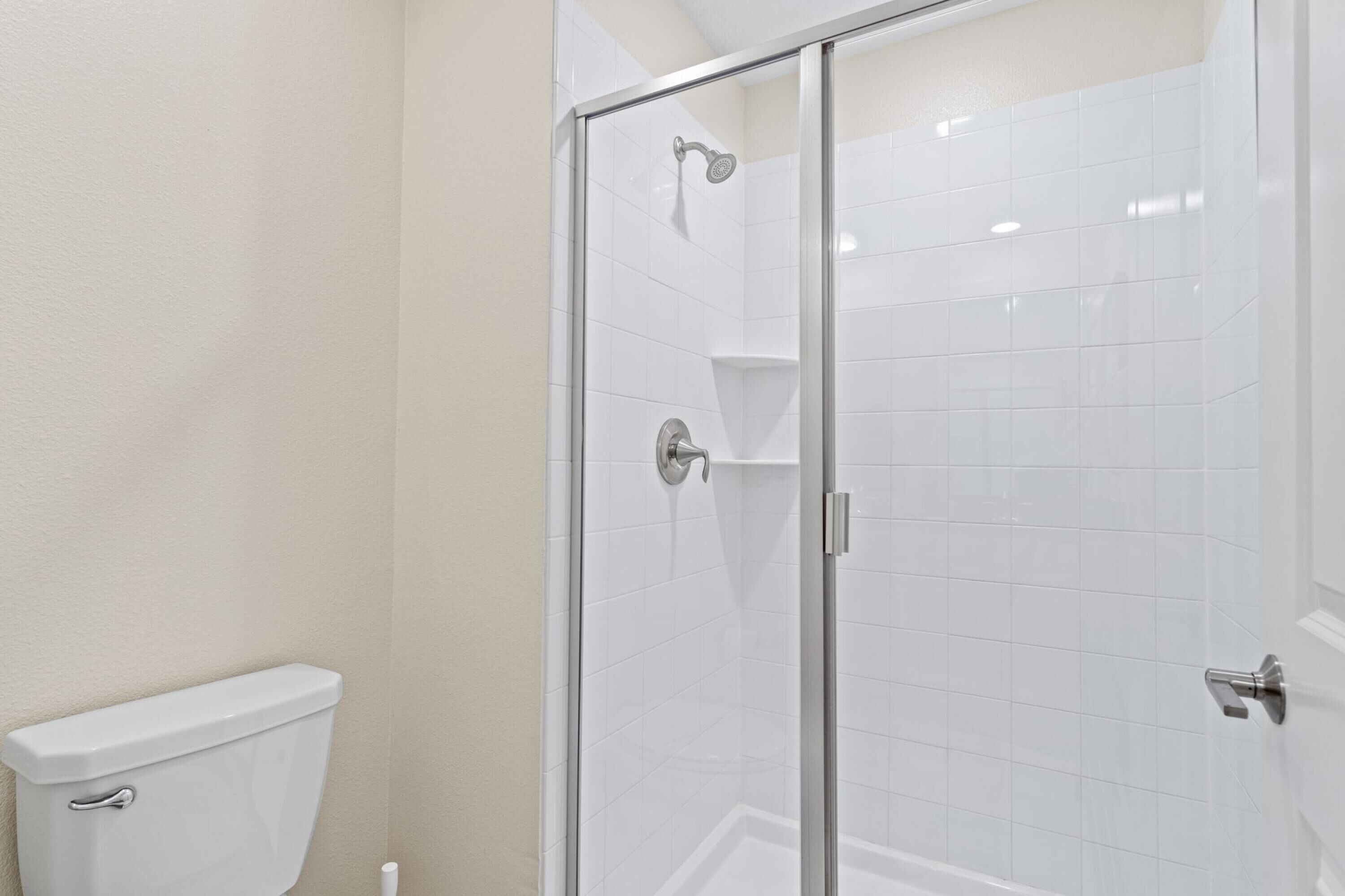 Une salle de bain avec une douche à parois de verre, des murs recouverts de carreaux blancs et des toilettes.
