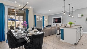 A modern living room with a dining area, a kitchen island, and a TV. - Champions Gate Oasis 4BR Vacation Haven (Davenport)