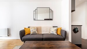 A modern living room with a grey sofa, two patterned throw pillows, a wooden coffee table, and a wall-mounted mirror. - Bright Battersea Apartment (London)